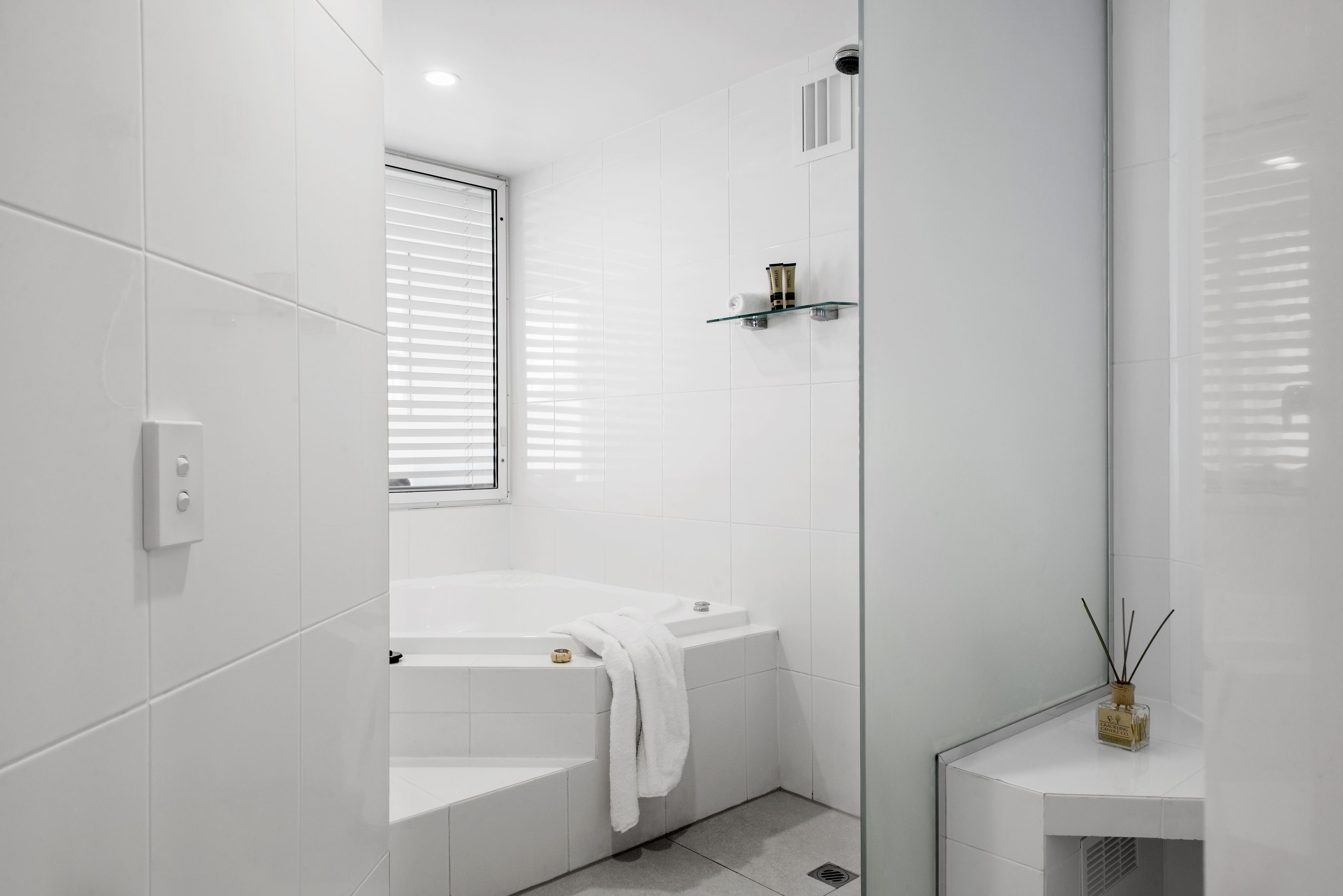 A modern bathroom with a white bathtub, a glass shower enclosure, and a small vanity with a bottle of reed diffuser.
