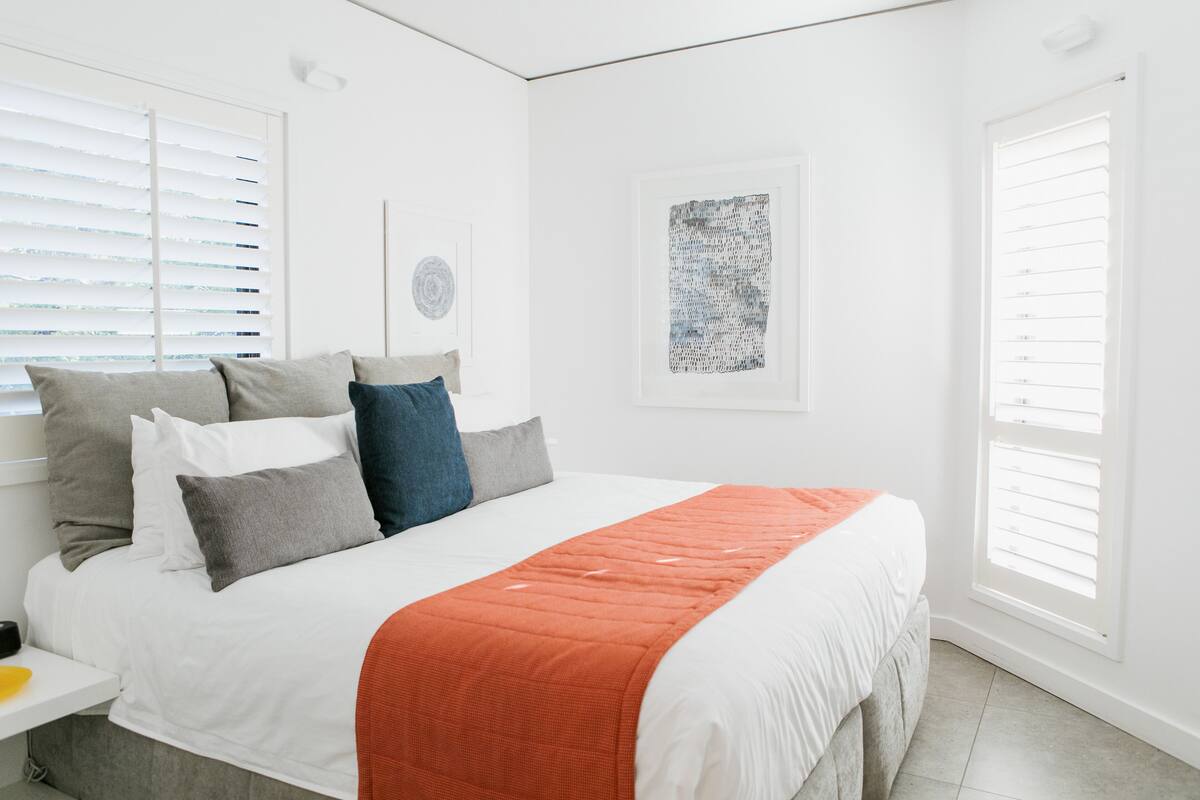 A modern bedroom with a large bed, white walls, and a single artwork on the wall.