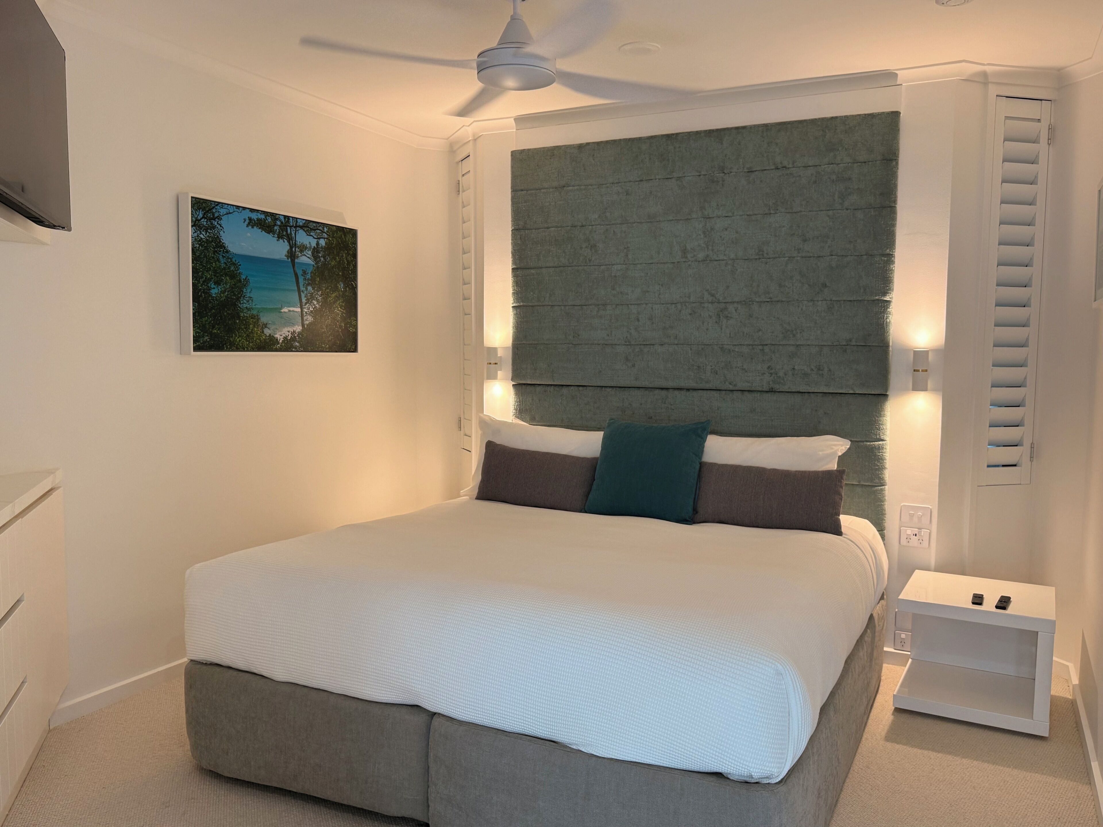A bedroom with a bed, a ceiling fan, a nightstand, and a wall-mounted light.