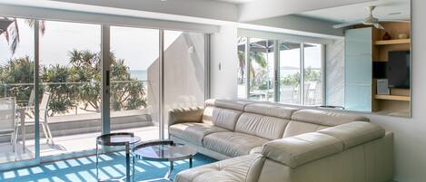 A modern living room with a beige sectional sofa, a glass coffee table, and a ceiling fan.