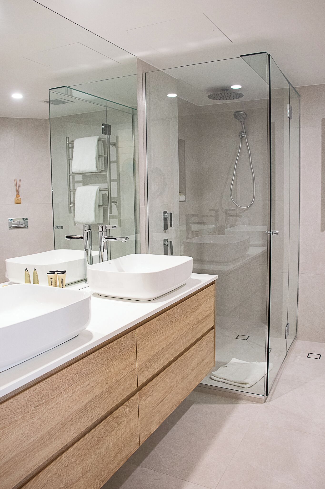 A modern bathroom with two white sinks, a glass-enclosed shower, and a wooden vanity.
