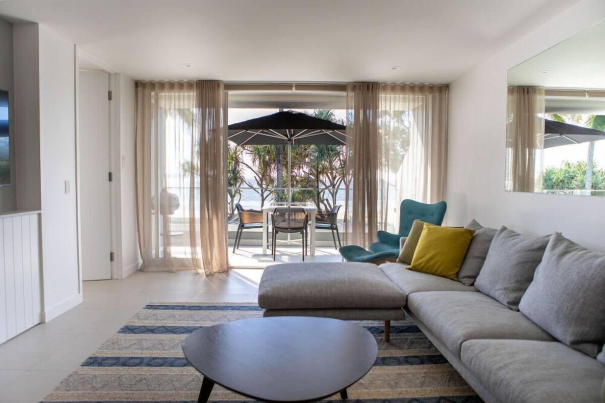 A modern living room with a sofa, ottoman, and a coffee table. There is a dining area with a table and chairs, and a large umbrella.