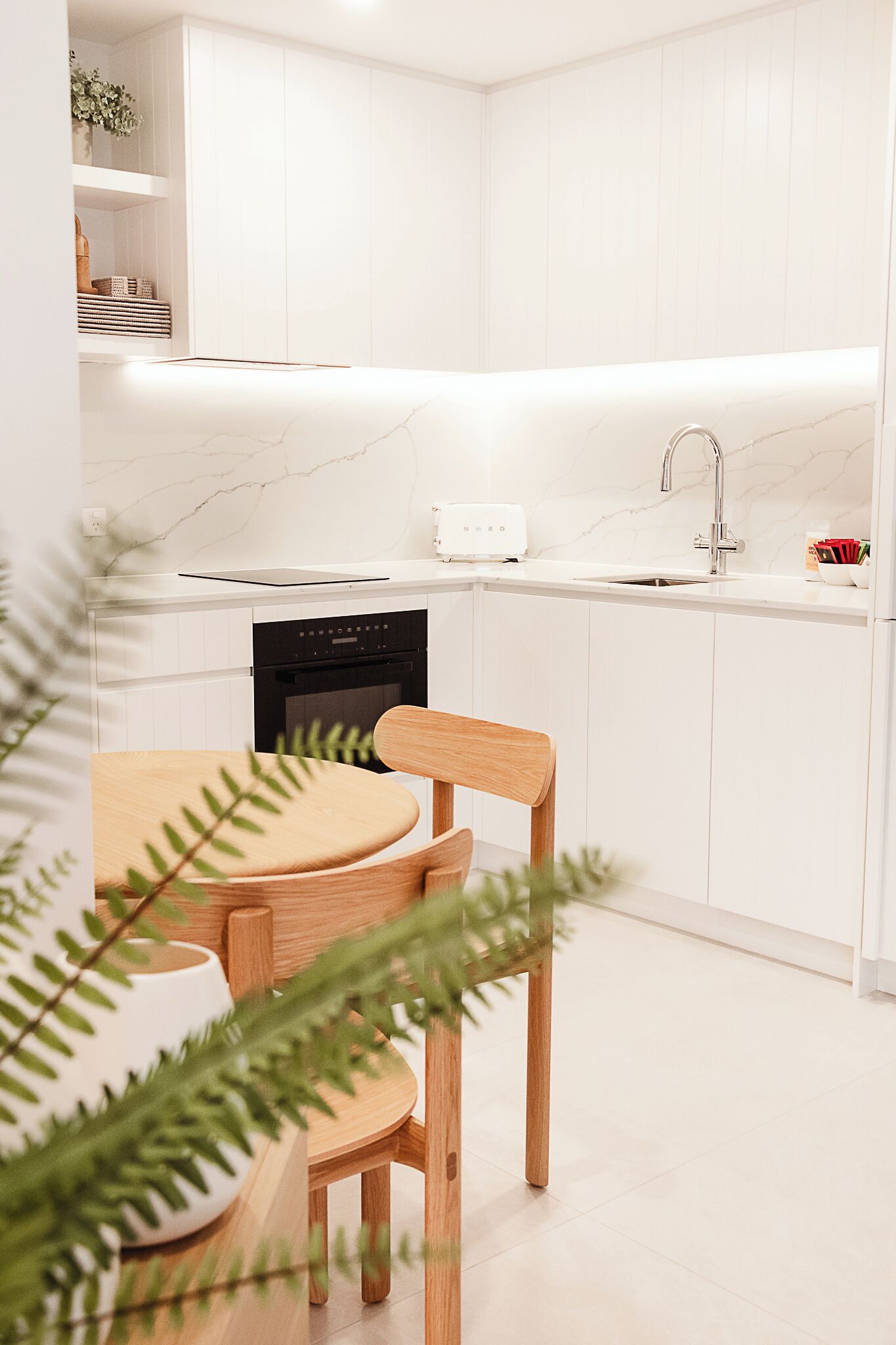A modern kitchen with white cabinetry, a black dishwasher, and a wooden dining table with chairs.