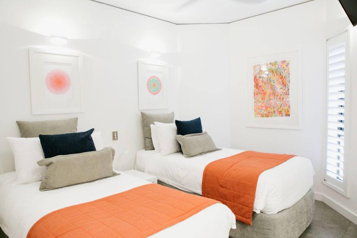 A hotel room with two beds, white walls, and artwork on the walls.