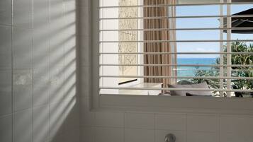 A modern bathroom with a large bathtub, a window with blinds, and a view of the ocean.