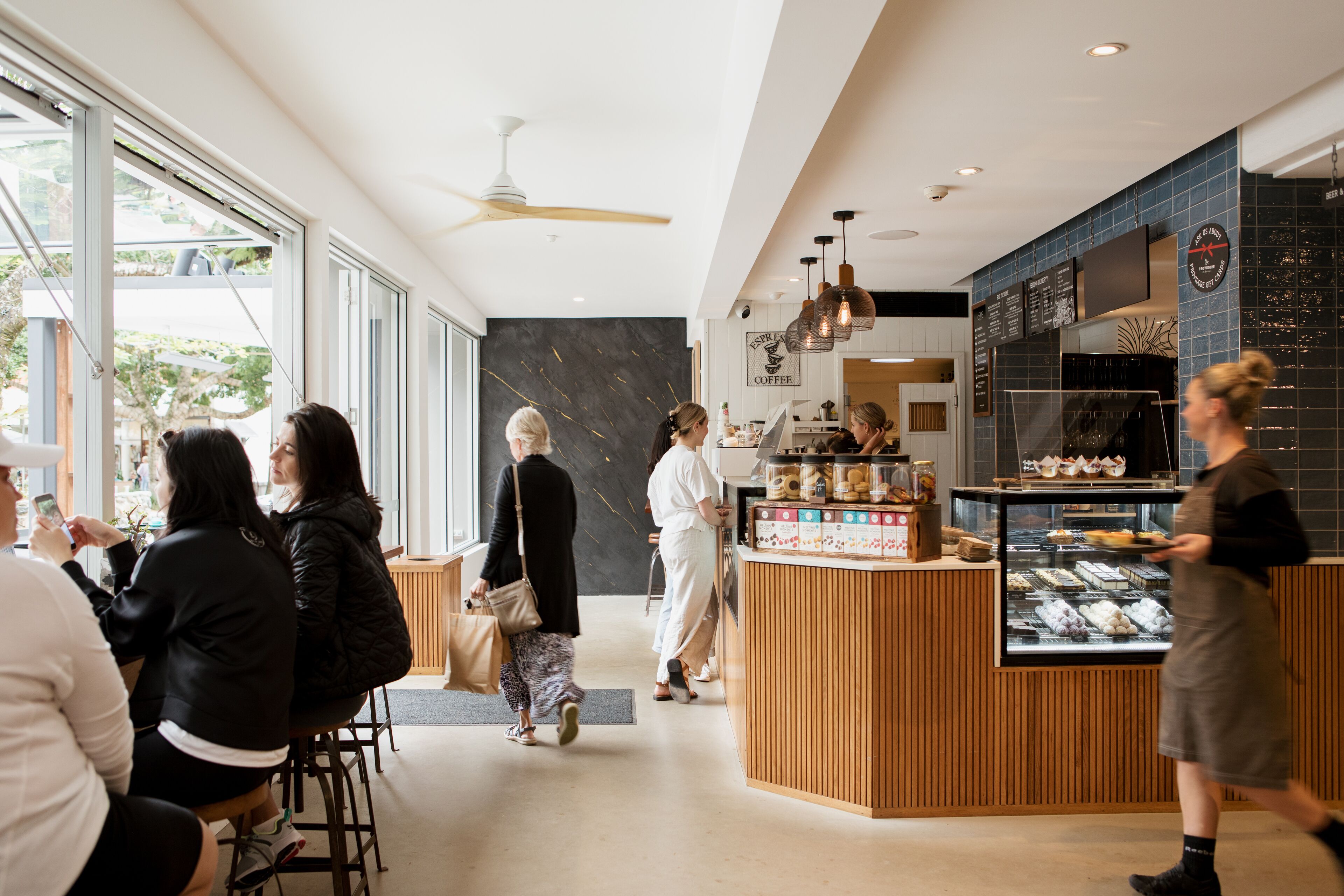 A modern café interior with large windows, a wooden counter, and a menu board.