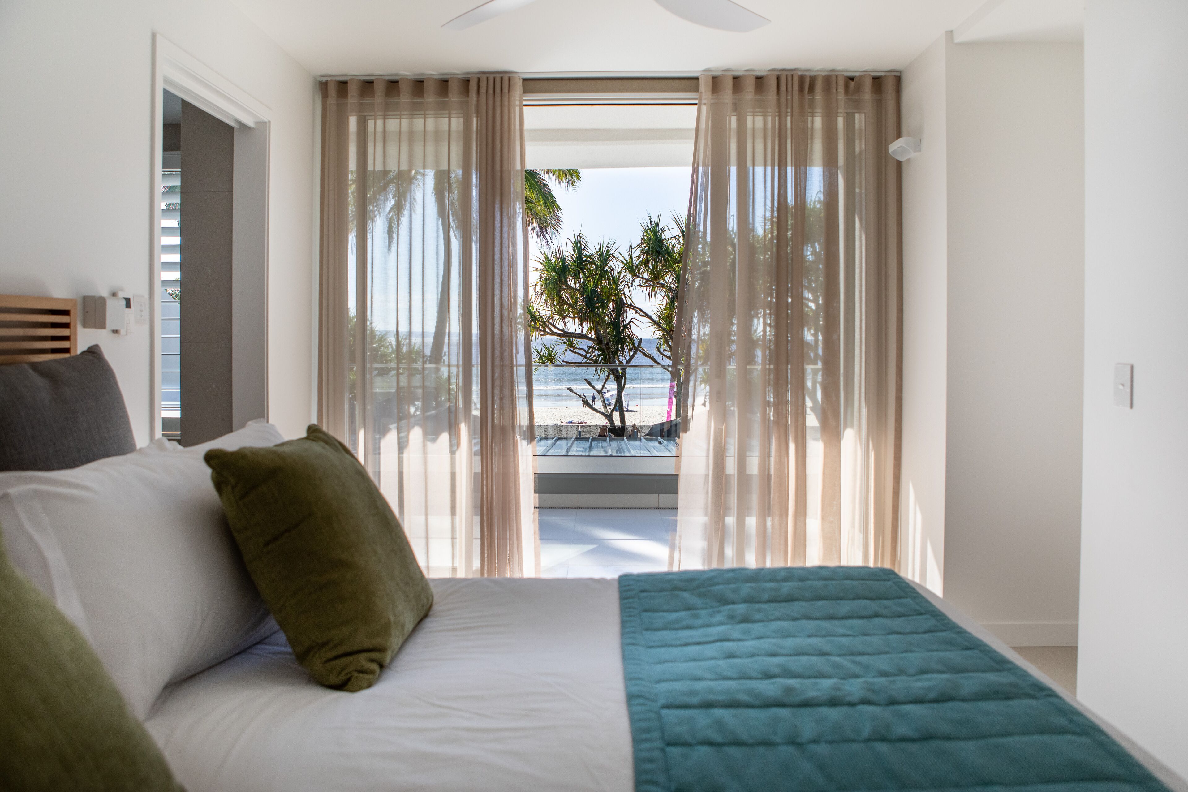A bedroom with a bed, a view of the beach, and sheer curtains.
