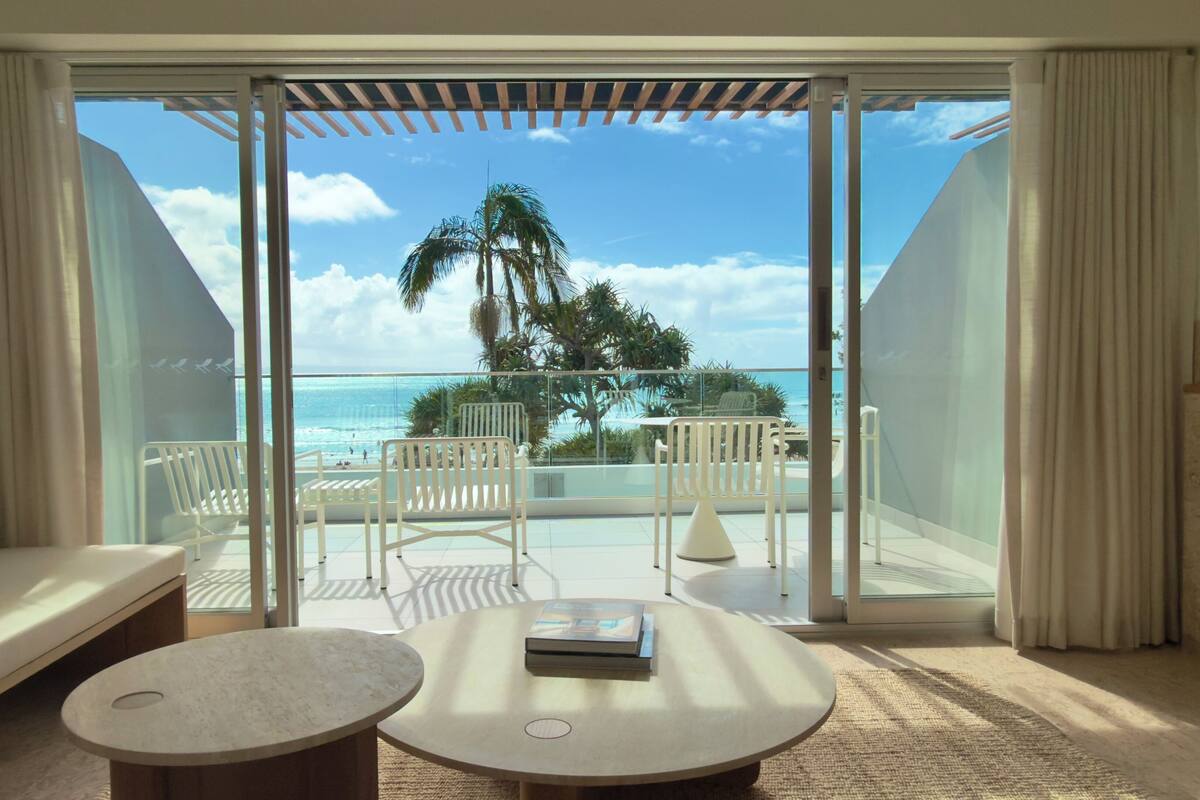 A hotel room with a balcony, a sofa, a coffee table, and a view of the ocean.