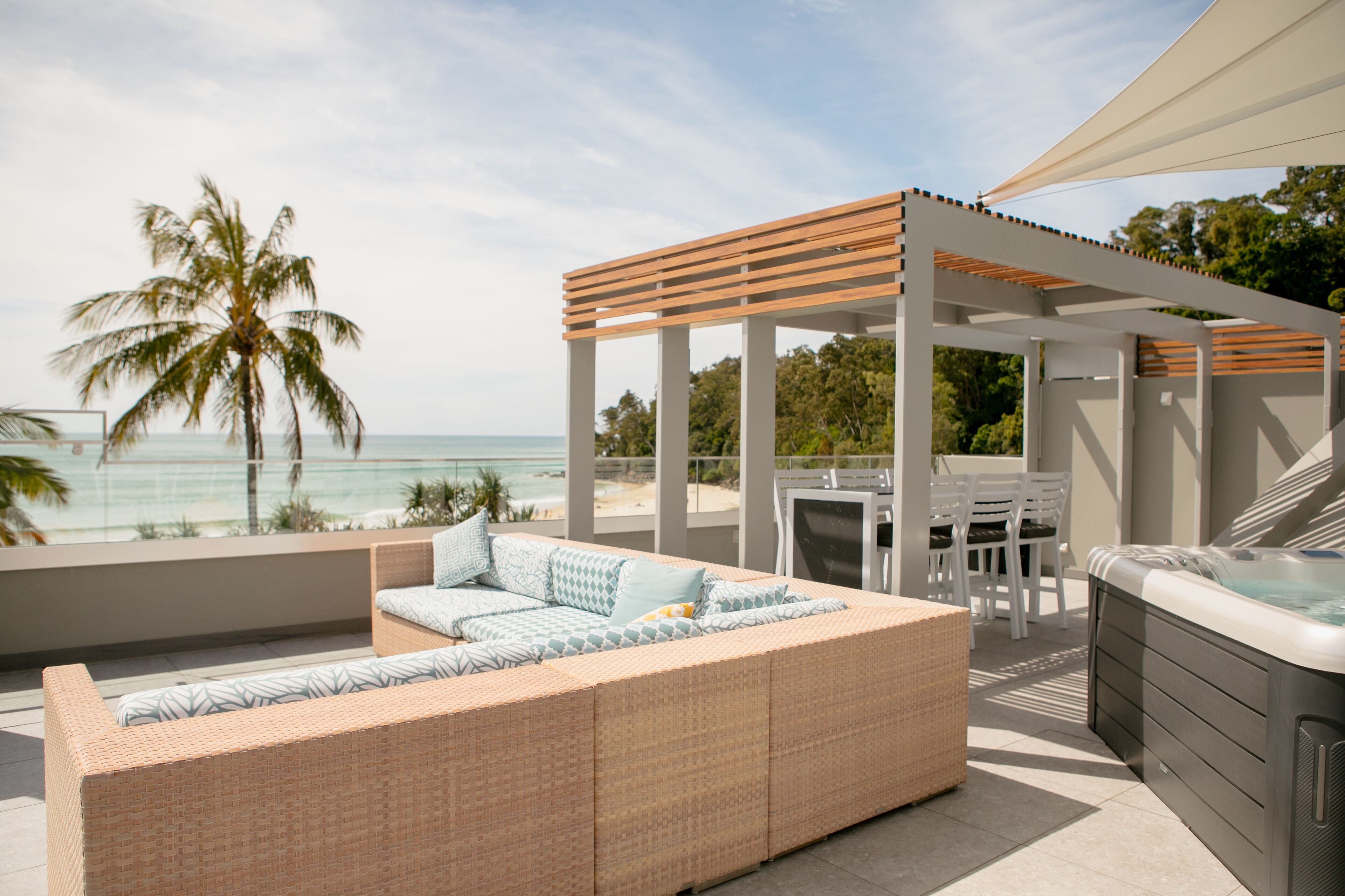 A rooftop patio with a wicker sofa, a hot tub, and a pergola overlooking the ocean.