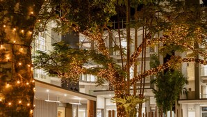 Een modern hotel met een ruim buitengebied, een stenen plantenbak met planten, en een auto ervoor geparkeerd.