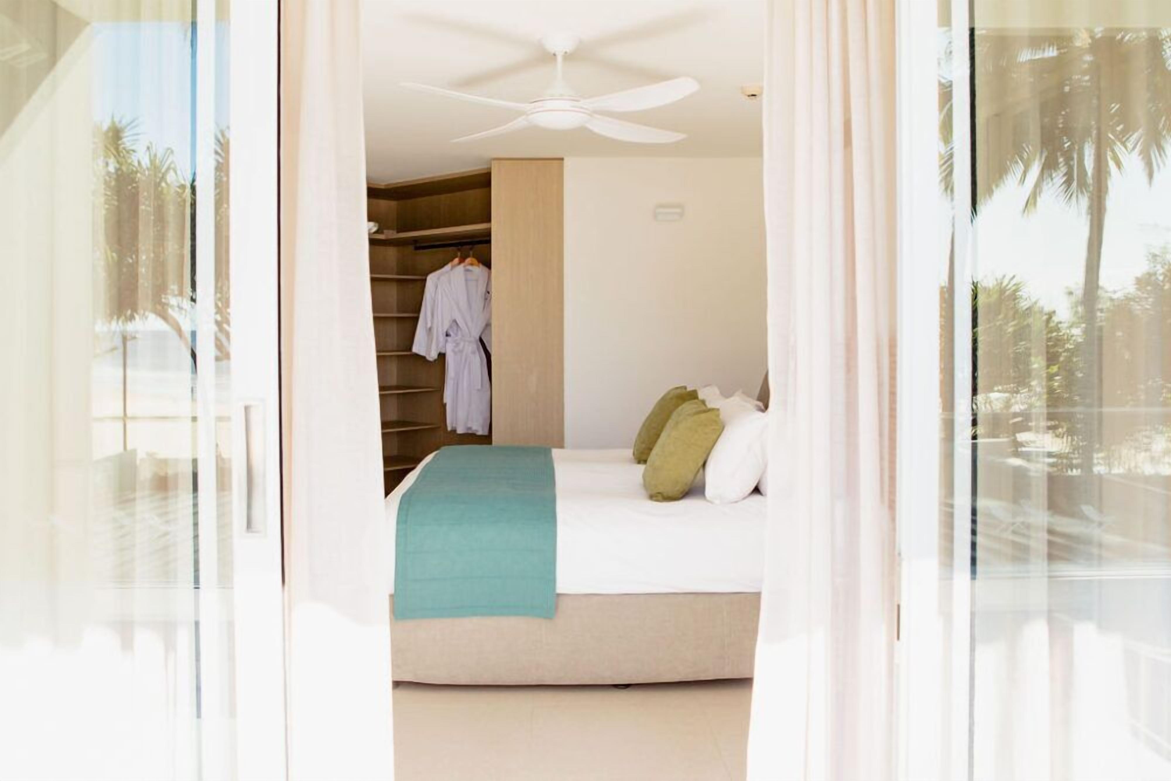 A bedroom with a bed, a ceiling fan, and a view of a closet with clothes.