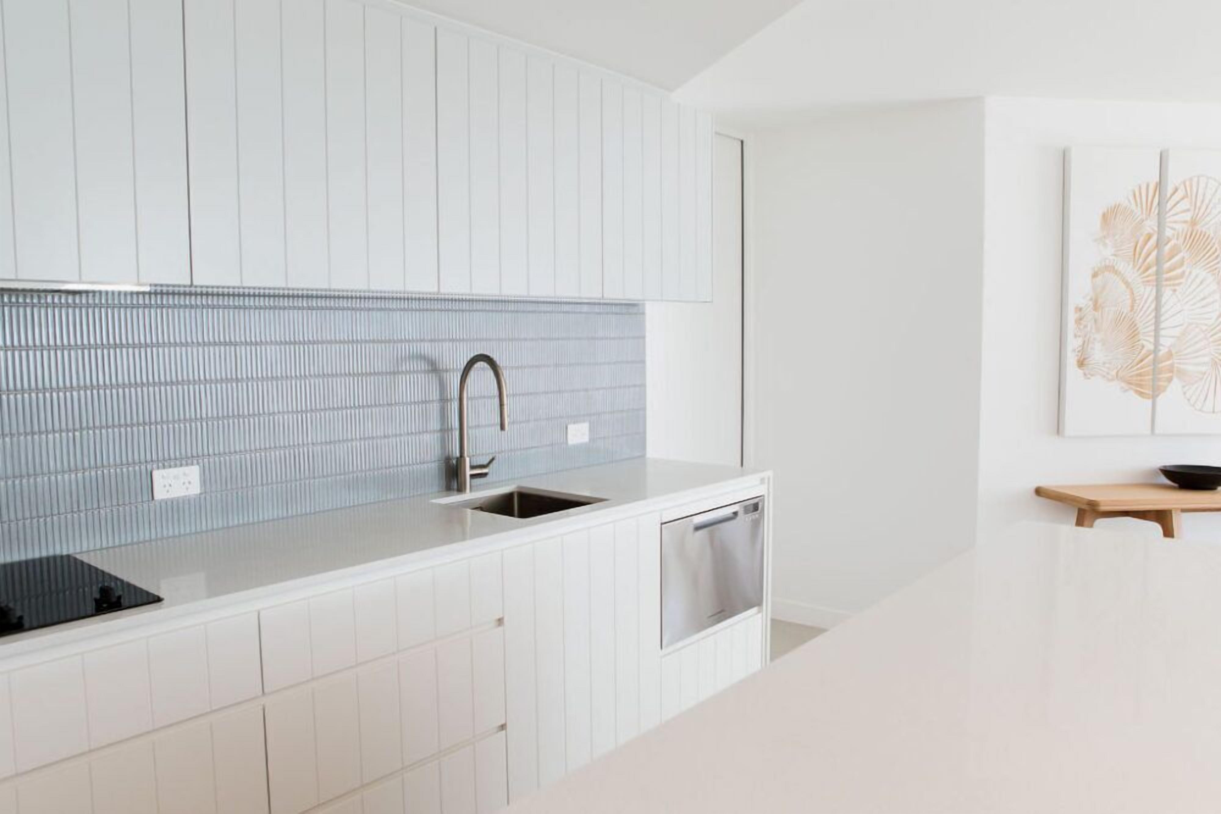A modern kitchen with white cabinetry, a stainless steel sink, and a blue backsplash.