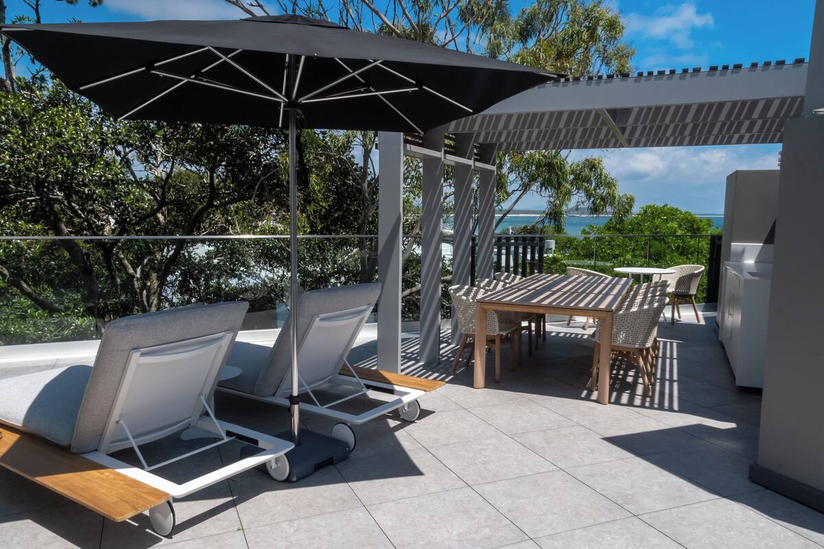 An outdoor patio with a table and chairs, a covered seating area, and a view of the sea.