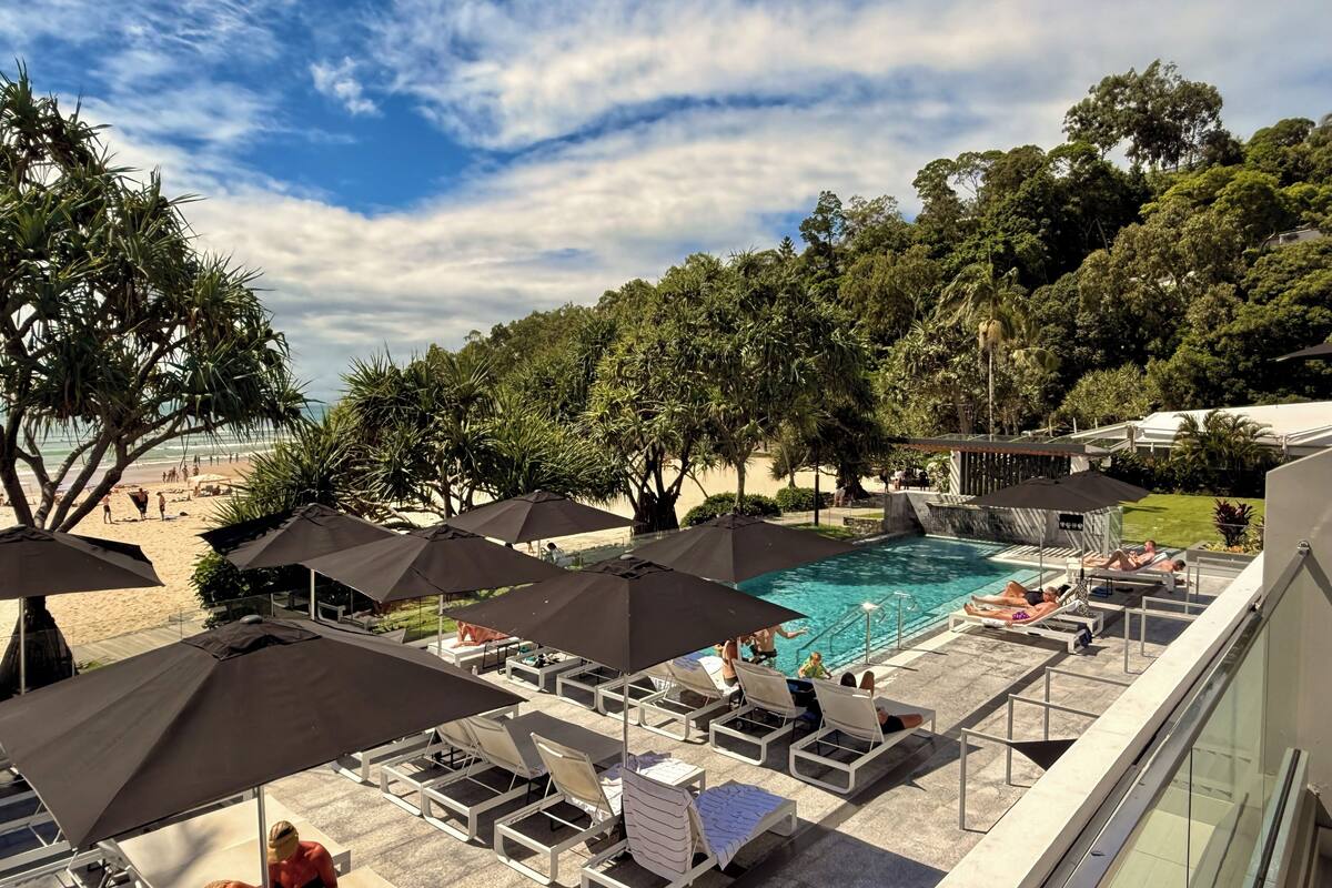 A poolside area with lounge chairs and umbrellas, a swimming pool, and a beach in the background.