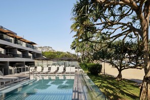 Ein moderner Poolbereich mit Liegestühlen und Sonnenschirmen, umgeben von Palmen und einem Gebäude mit Balkonen.