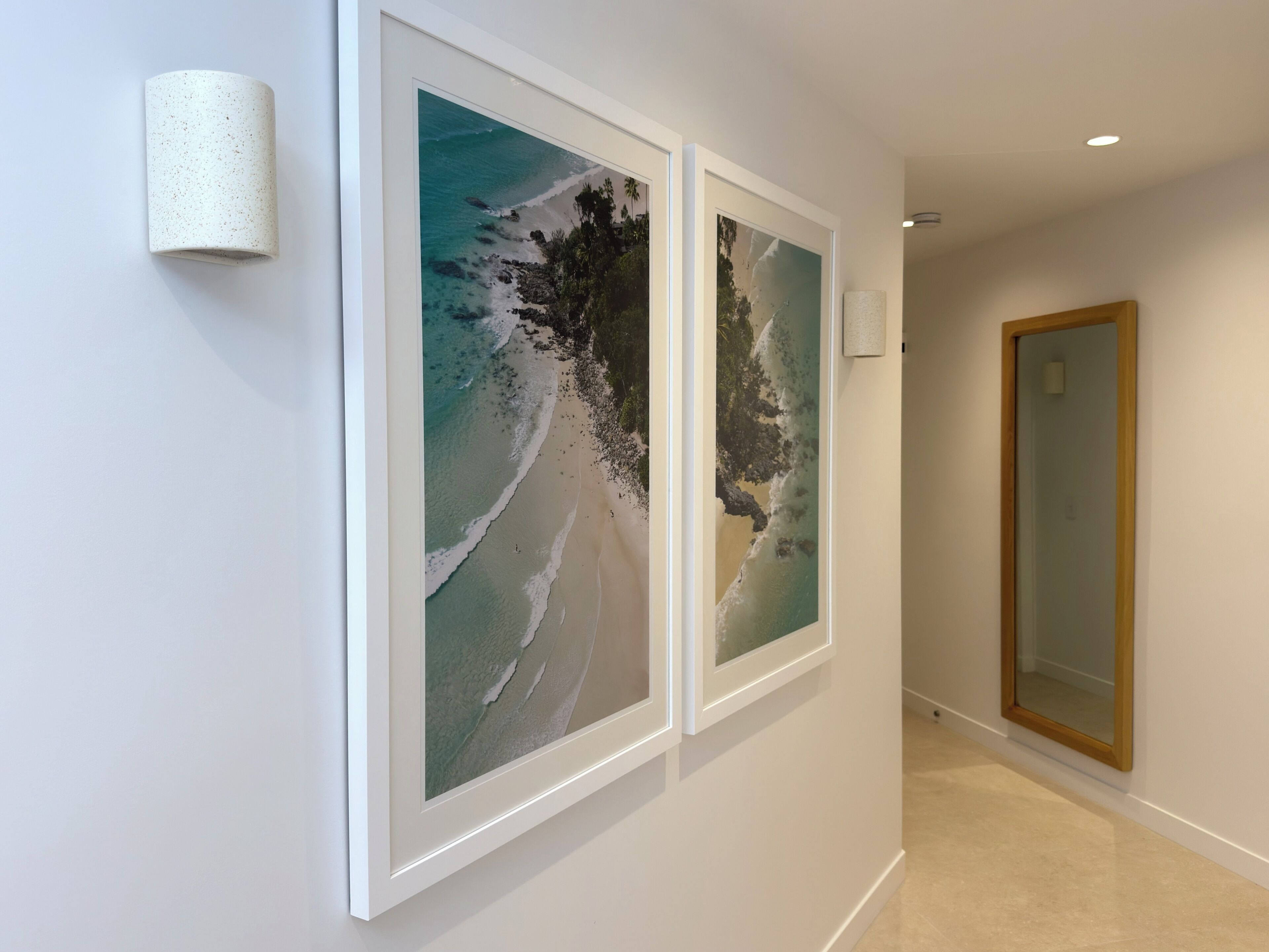 A hallway with two framed beach photographs on the wall, a light fixture, and a wooden door.