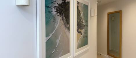 A hallway with two framed beach photographs on the wall, a light fixture, and a wooden door.