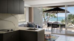 Een moderne keuken met een groot eiland, een eethoek met tafel en stoelen, en een balkon met uitzicht op de oceaan.