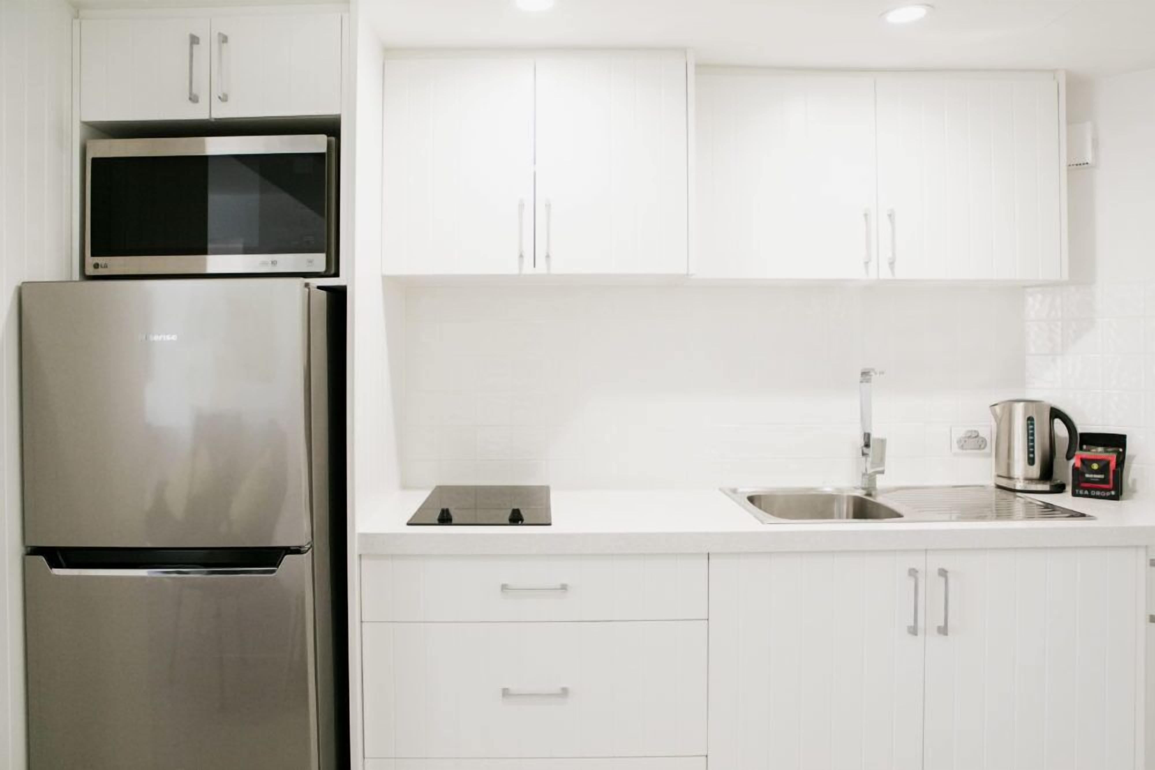 A modern kitchen with white cabinets, a stainless steel refrigerator, a microwave, and a kettle.