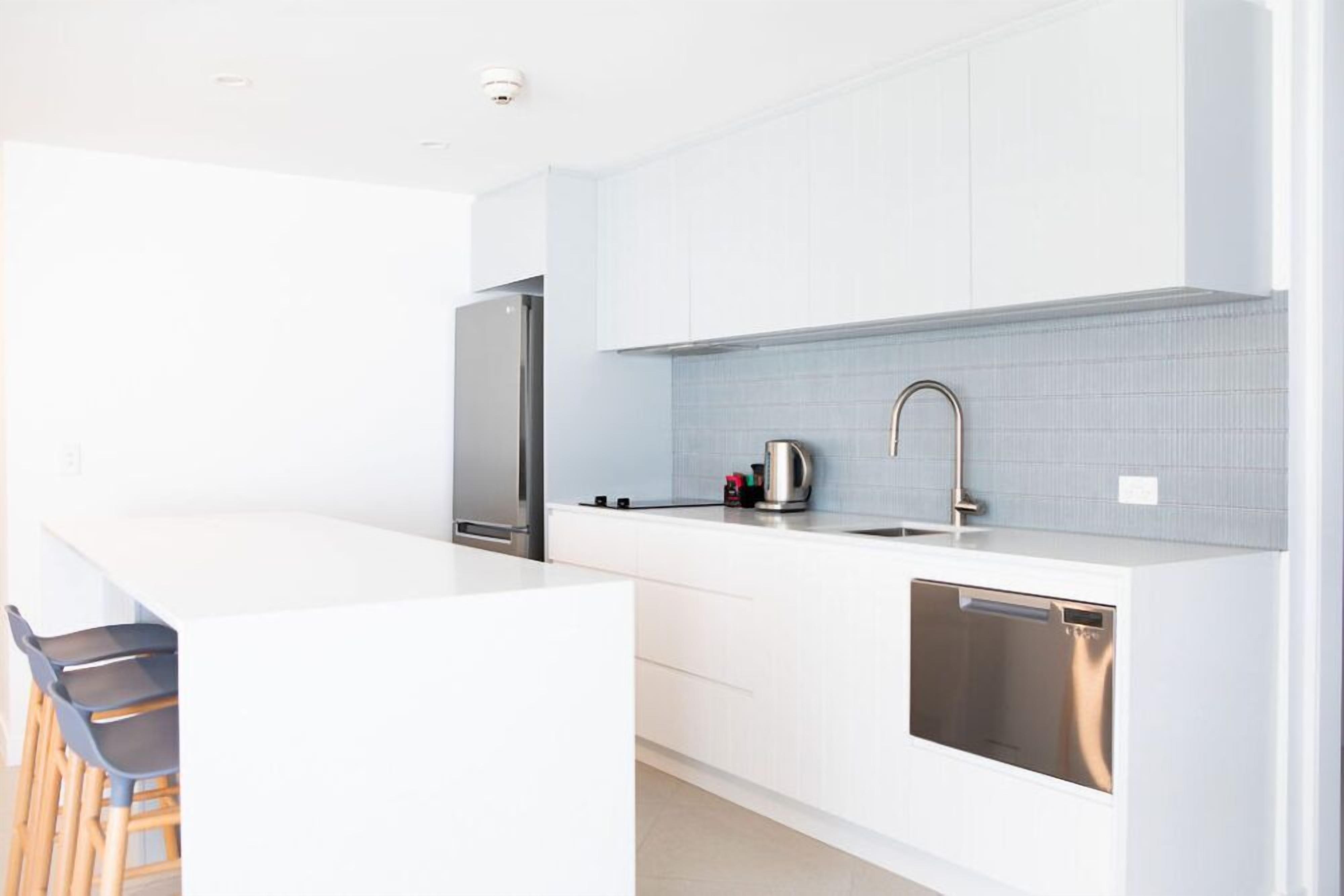 A modern kitchen with white cabinetry, a stainless steel refrigerator, and a built-in dishwasher.