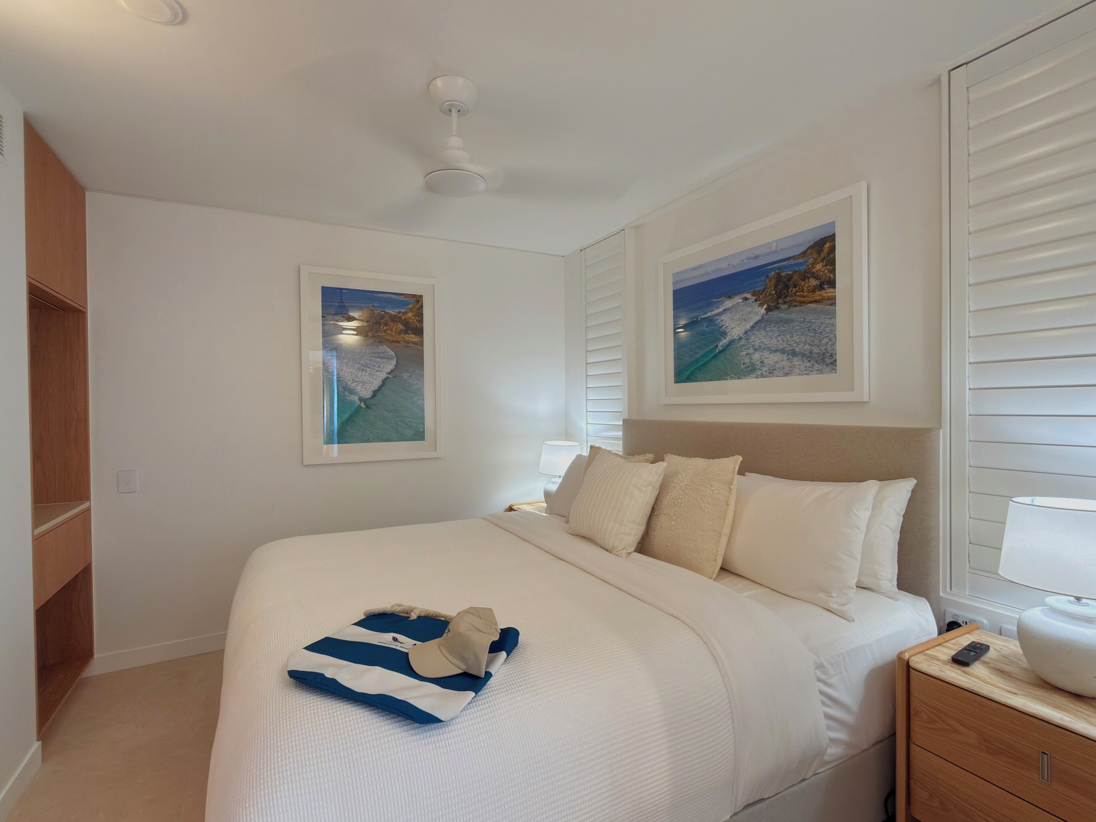 Quarto com cama, mesa de cabeceira, abajur e duas imagens emolduradas na parede.