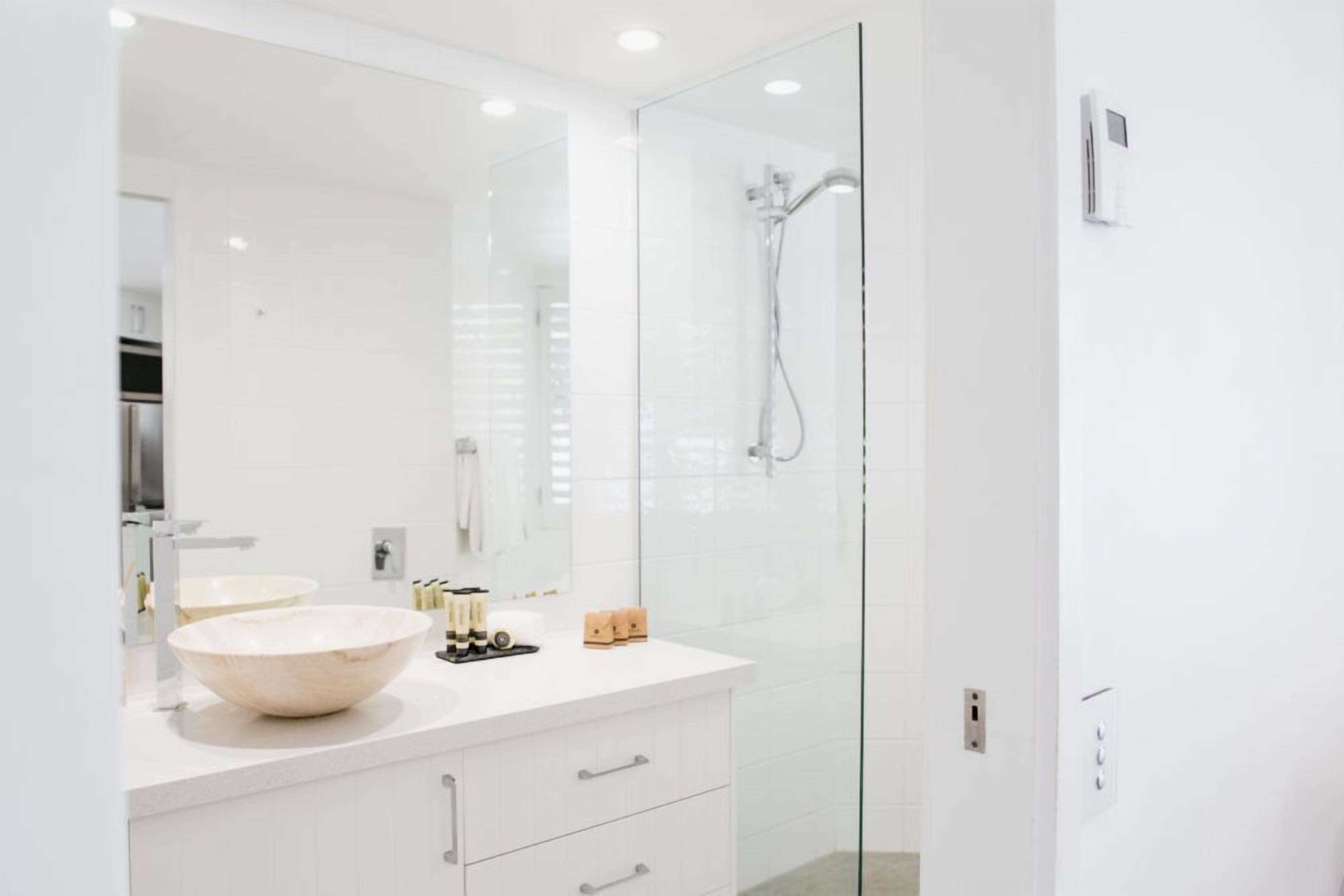A modern bathroom with a large mirror, two sinks, and a glass-enclosed shower.