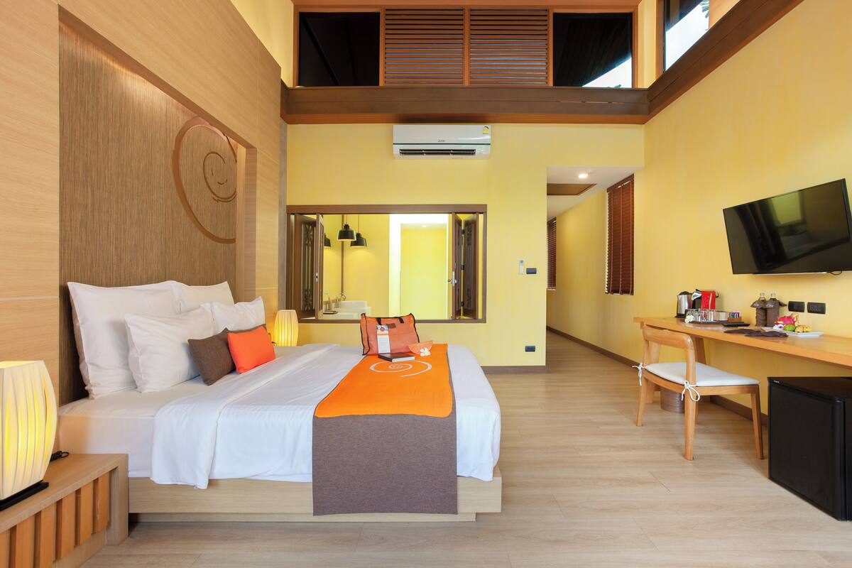 A hotel room with a bed, a desk, a TV, and an air conditioning unit.