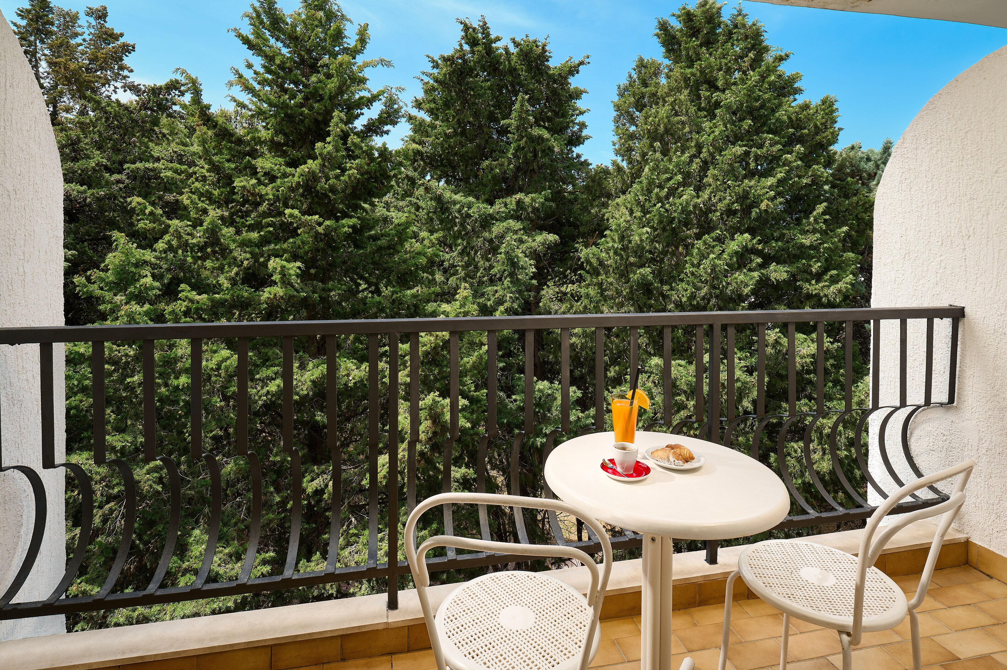 Ein Balkon mit rundem Tisch und zwei Stühlen, mit Blick auf einen dichten Wald.