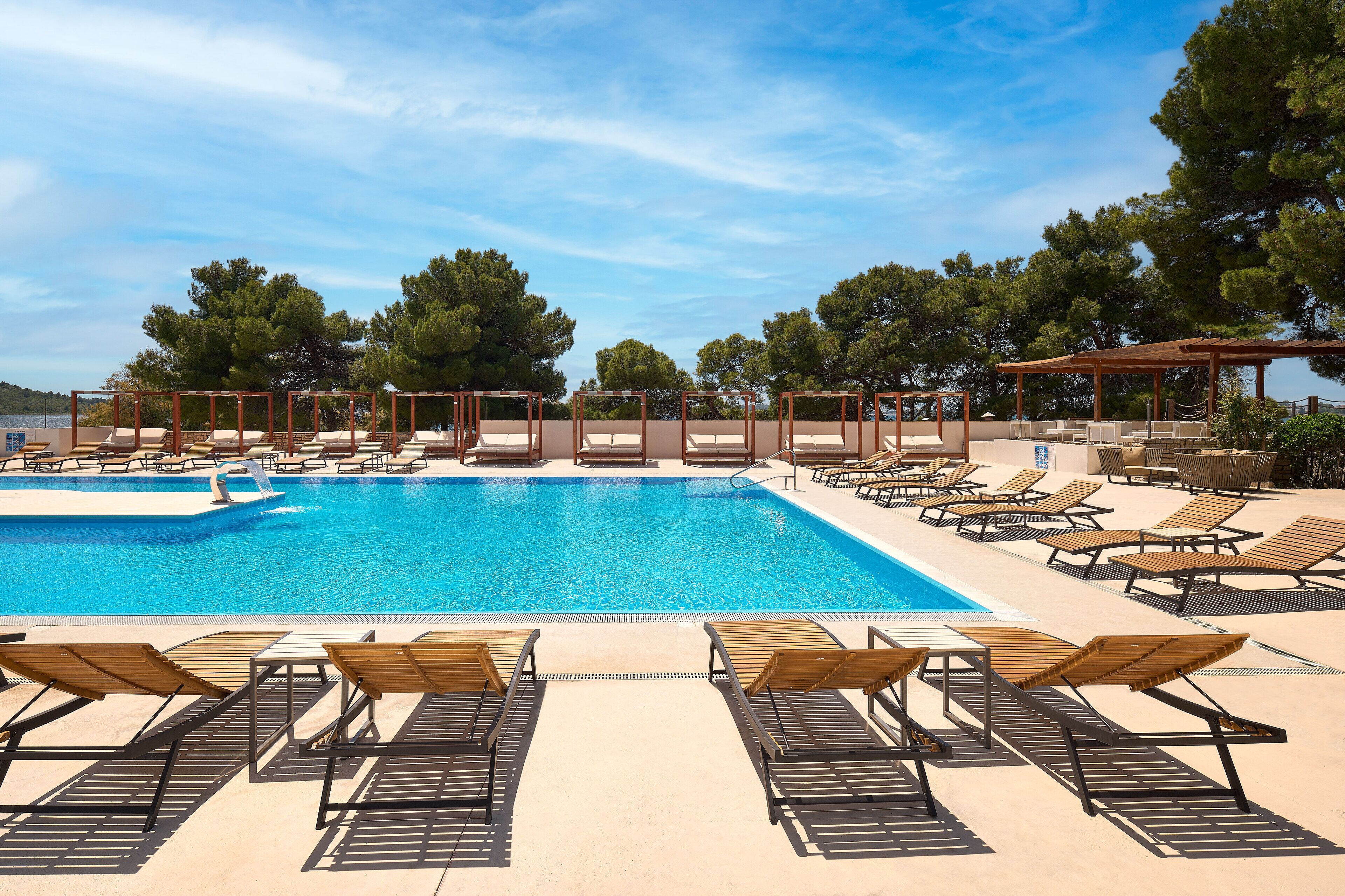 Une piscine entourée d’arbres, avec des chaises longues et des parasols.