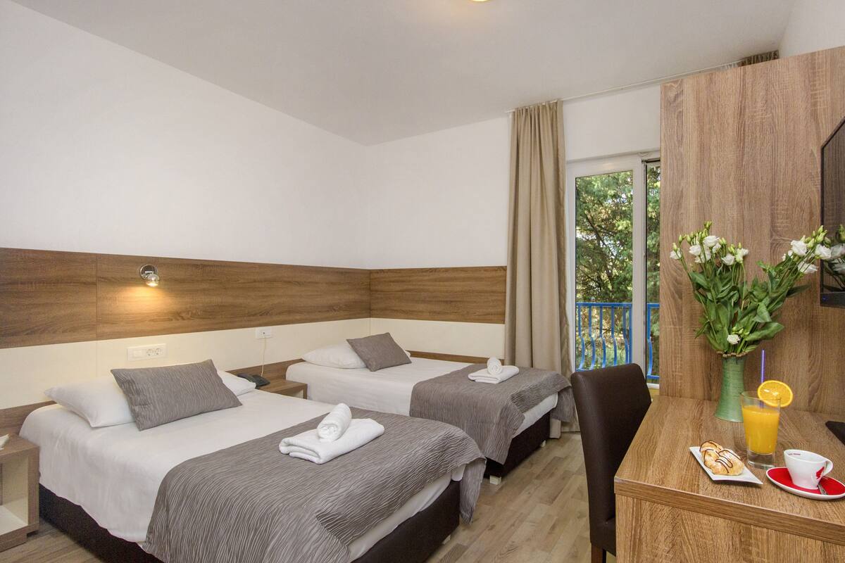 Habitación de hotel con dos camas, una mesa de comedor con desayuno y vistas al exterior.