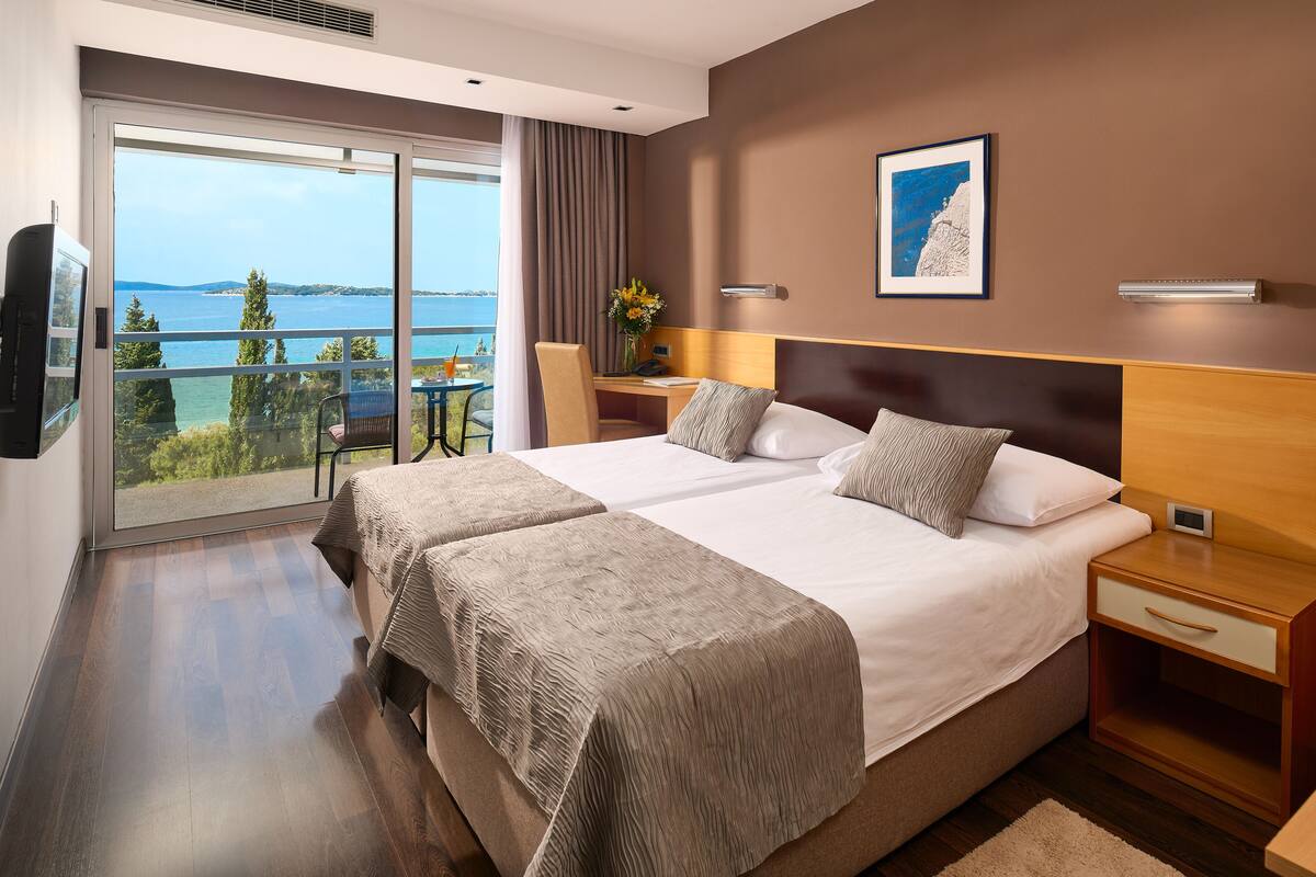 Habitación de hotel con una cama grande, un escritorio con silla, televisor y vista al mar.