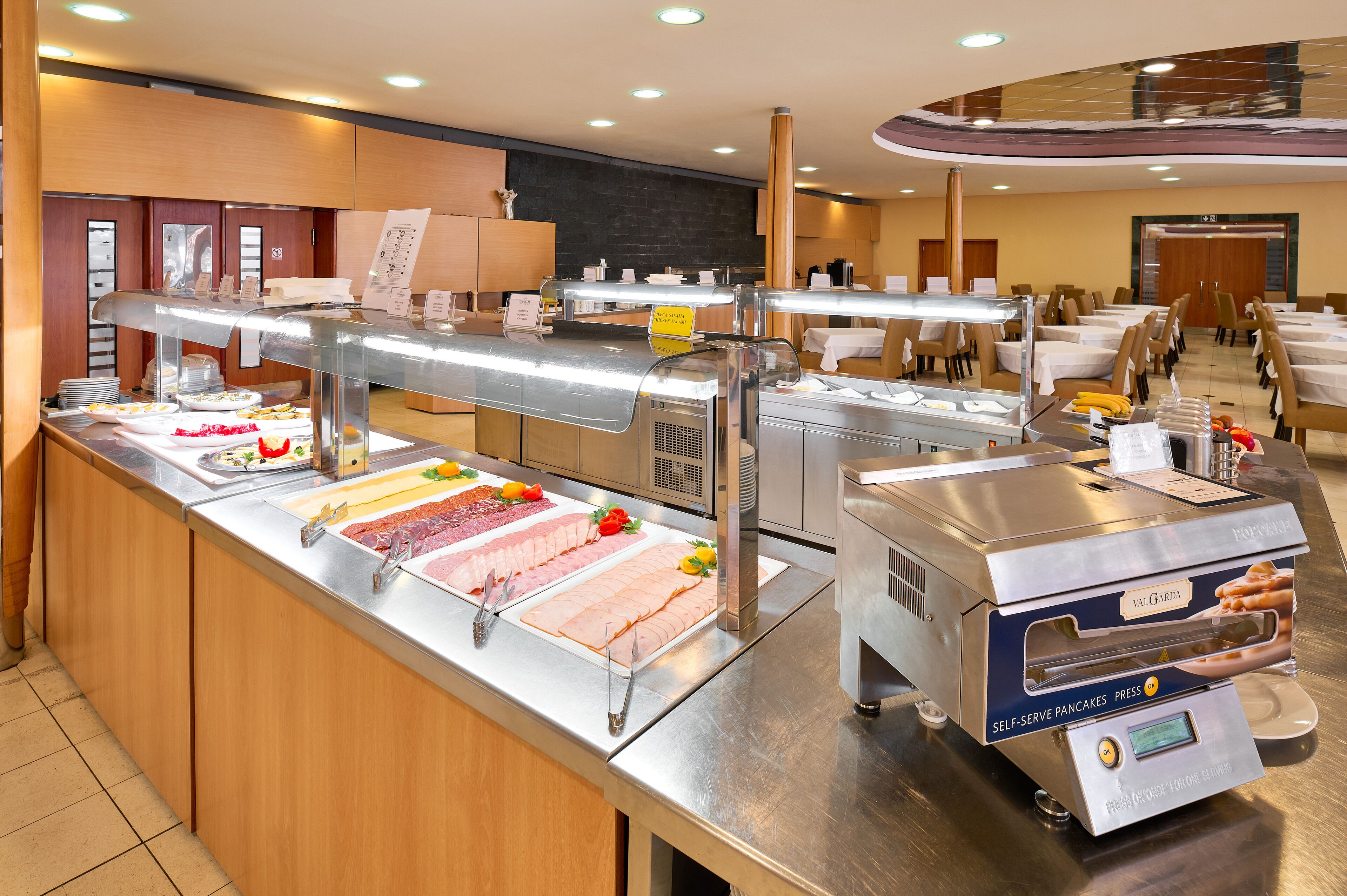 Un buffet proposant une variété de plats, un espace où l’on peut préparer soi-même des crêpes, et un coin repas avec des tables et des chaises.