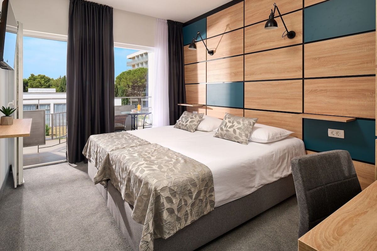 Una habitación de hotel moderna con una cama grande, un escritorio y vistas al exterior.