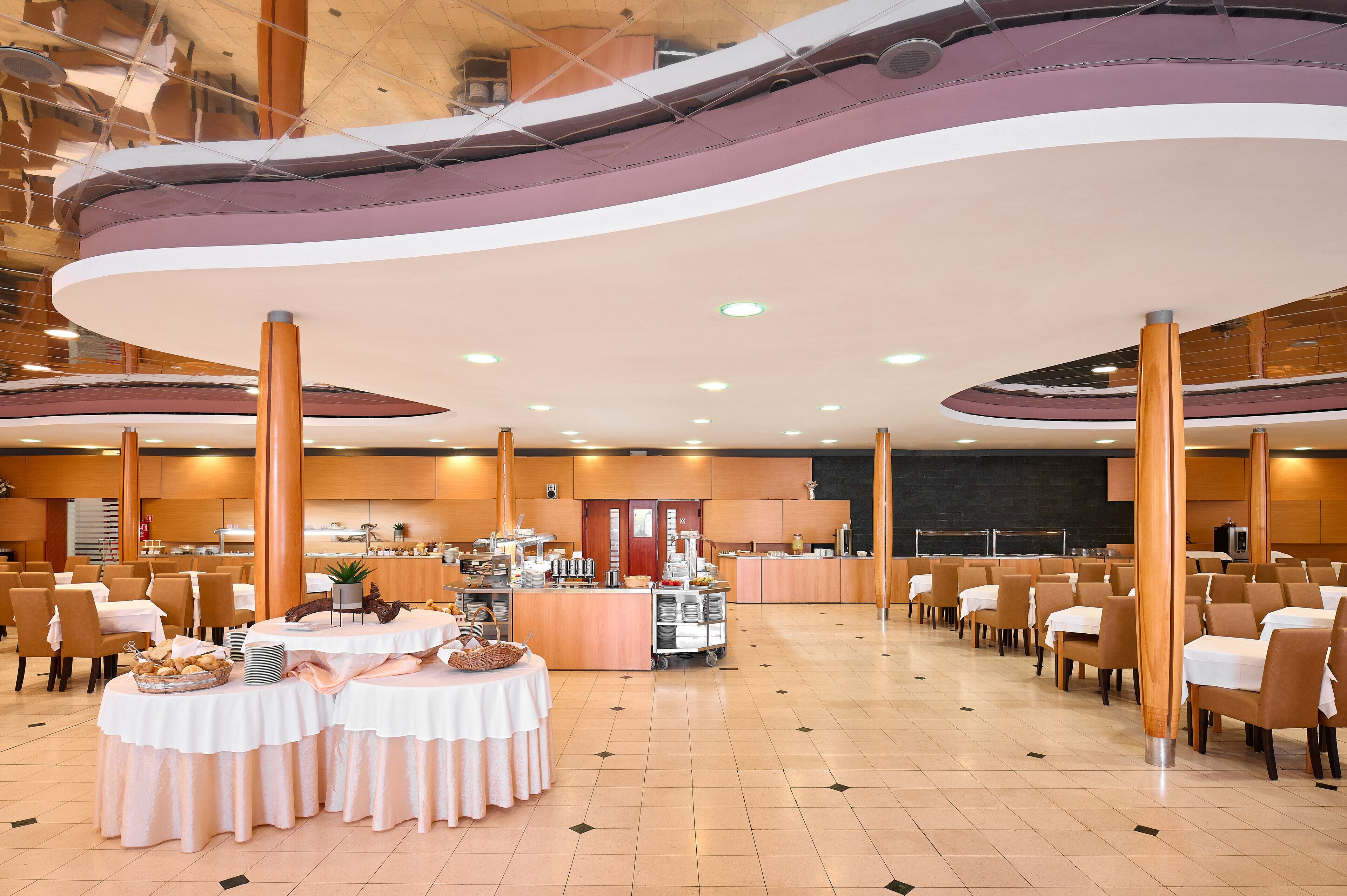 A spacious dining area with round tables, a buffet station, and a stage in the background.