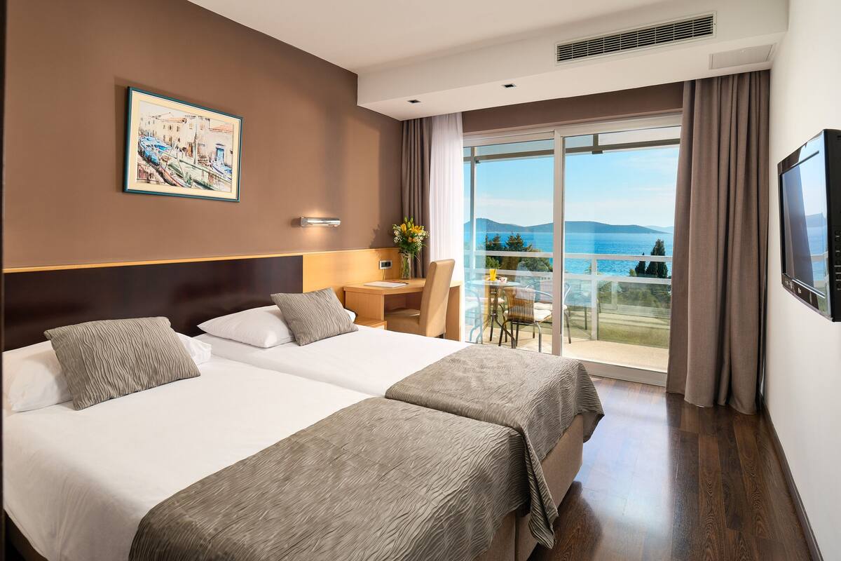 Habitación de hotel con una cama grande, un escritorio y un balcón con vista al mar.
