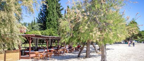 An outdoor café with wooden tables and chairs, a pergola, and a stone-paved area.