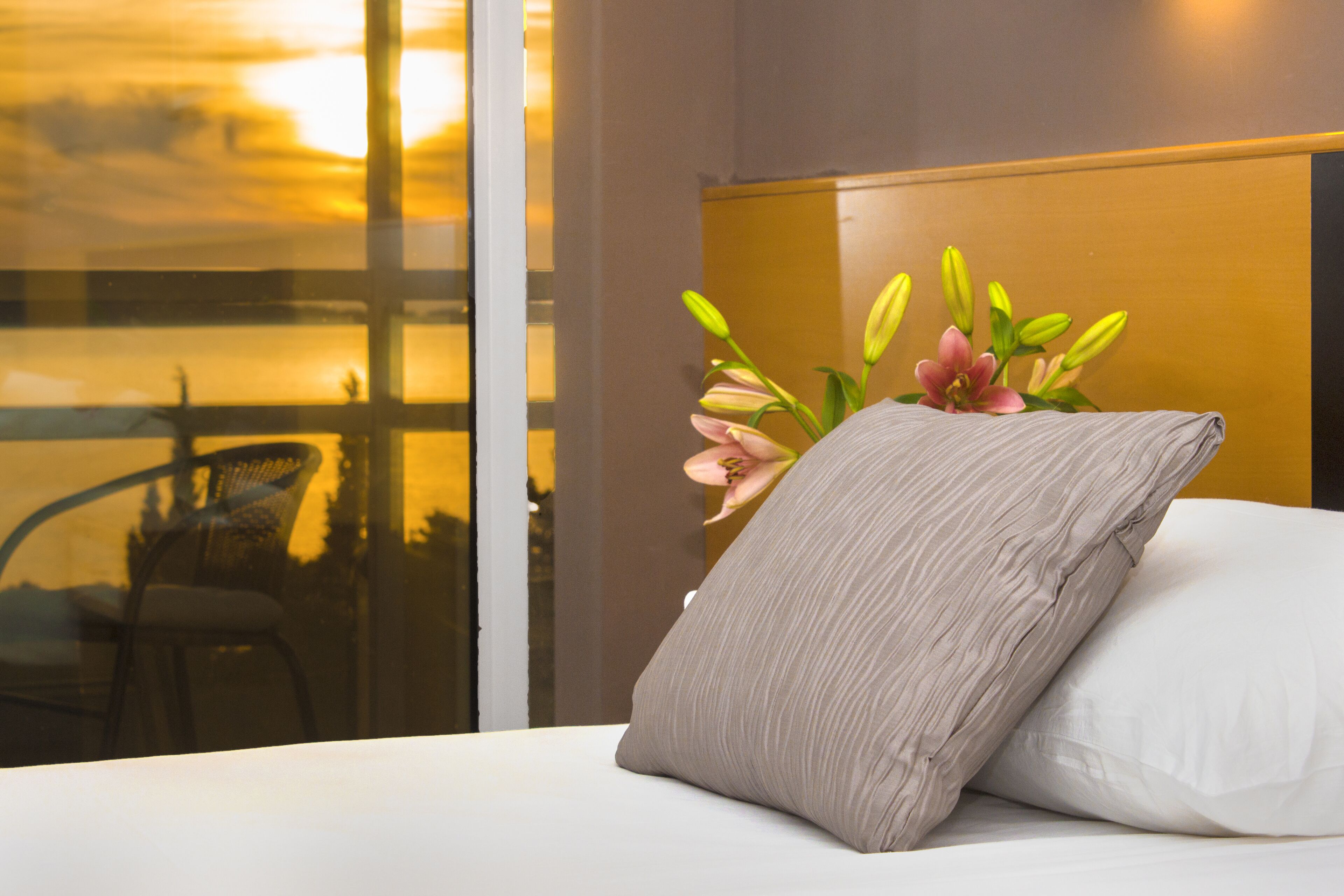 A hotel room with a bed, pillows, and a vase with flowers.