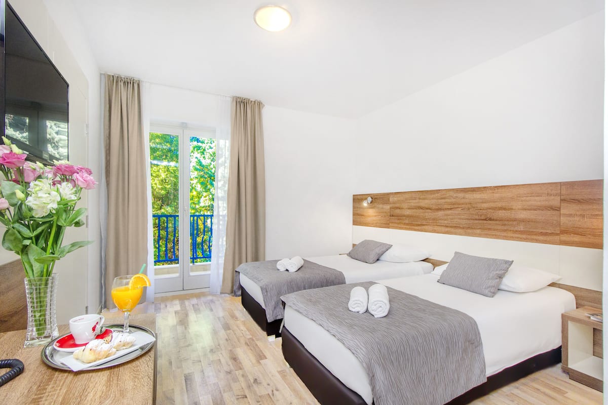 Habitación de hotel con dos camas, una bandeja de desayuno y vista a zonas verdes.