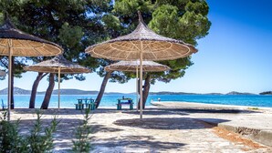 A beachside area with thatched umbrellas, stone seating, and a view of the sea. - Hotel Imperial Vodice (Vodice)