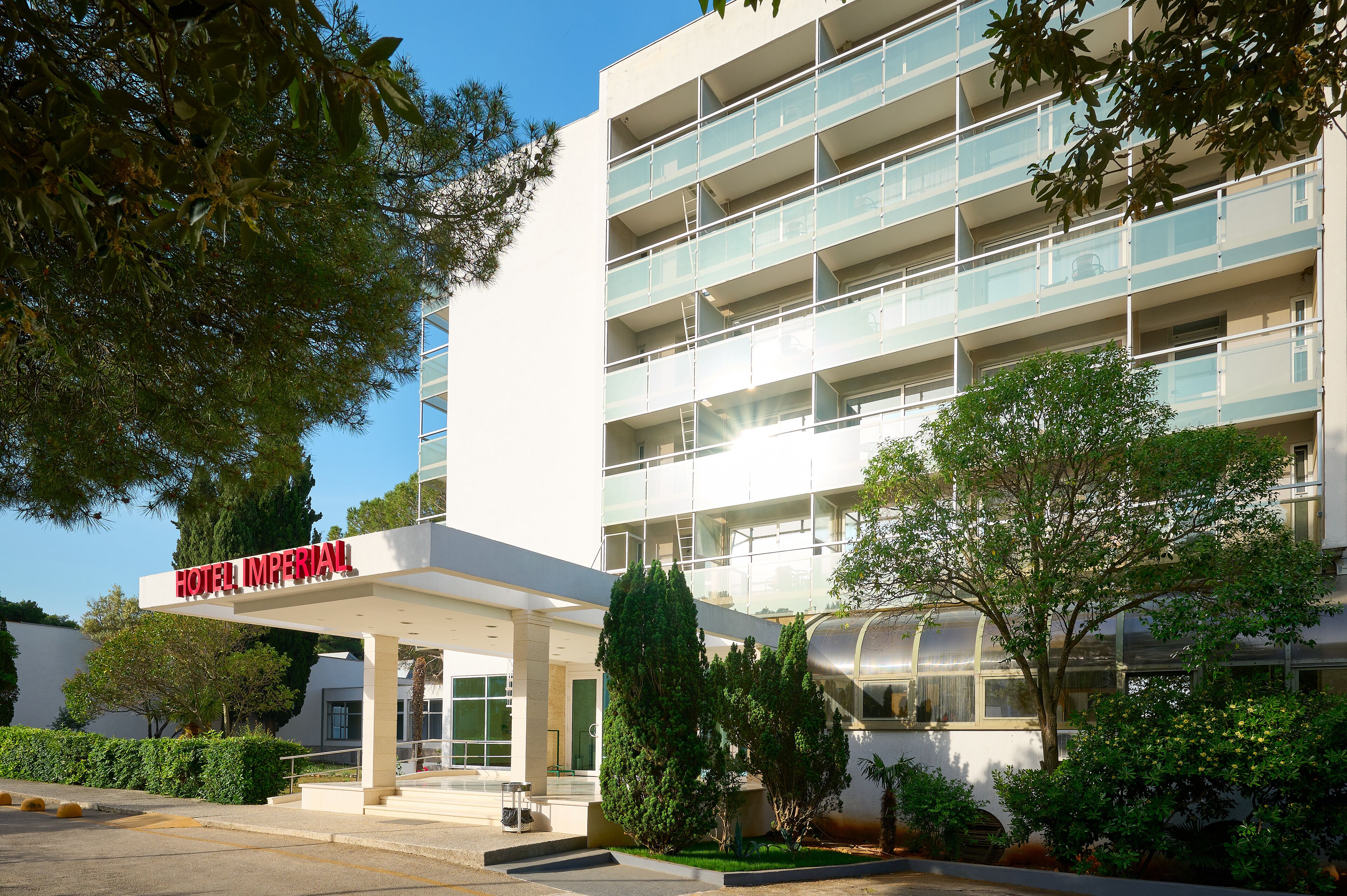 A modern hotel with a glass facade, multiple balconies, and a clear sky.
