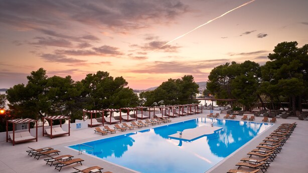 A rectangular pool with lounge chairs and umbrellas, surrounded by trees and a sunset sky. - Hotel Imperial Vodice (Vodice)