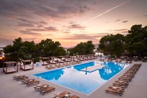 A rectangular pool with lounge chairs and umbrellas, surrounded by trees and a sunset sky. - Hotel Imperial Vodice (Vodice)