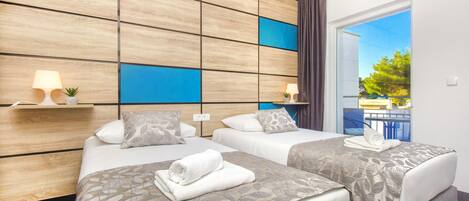 A hotel room with two beds, a wooden headboard, a balcony with a view, and a small plant on the nightstand.