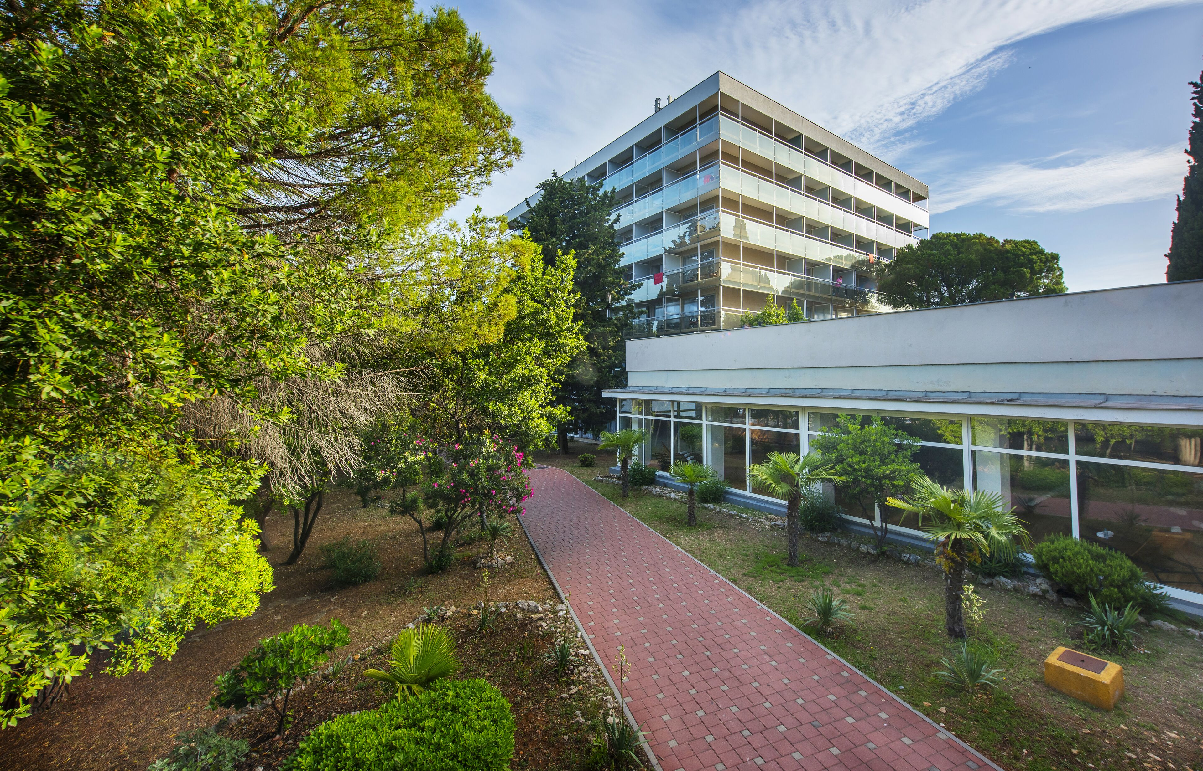 A modern building with a glass facade, surrounded by a landscaped garden with a paved walkway.