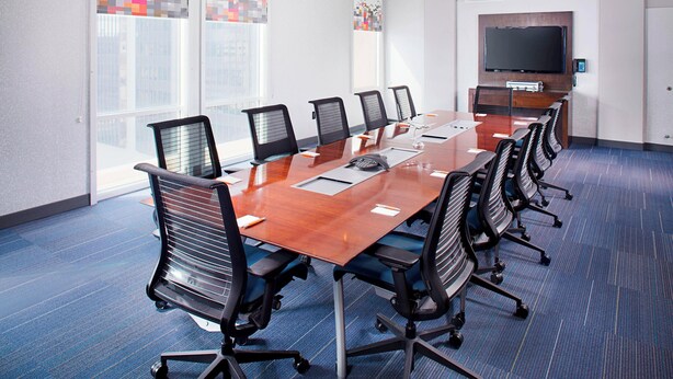 A conference room with a long table, multiple chairs, a flat-screen TV, and large windows with pixelated curtains. - Aloft by Marriott Charlotte City Center (Charlotte)