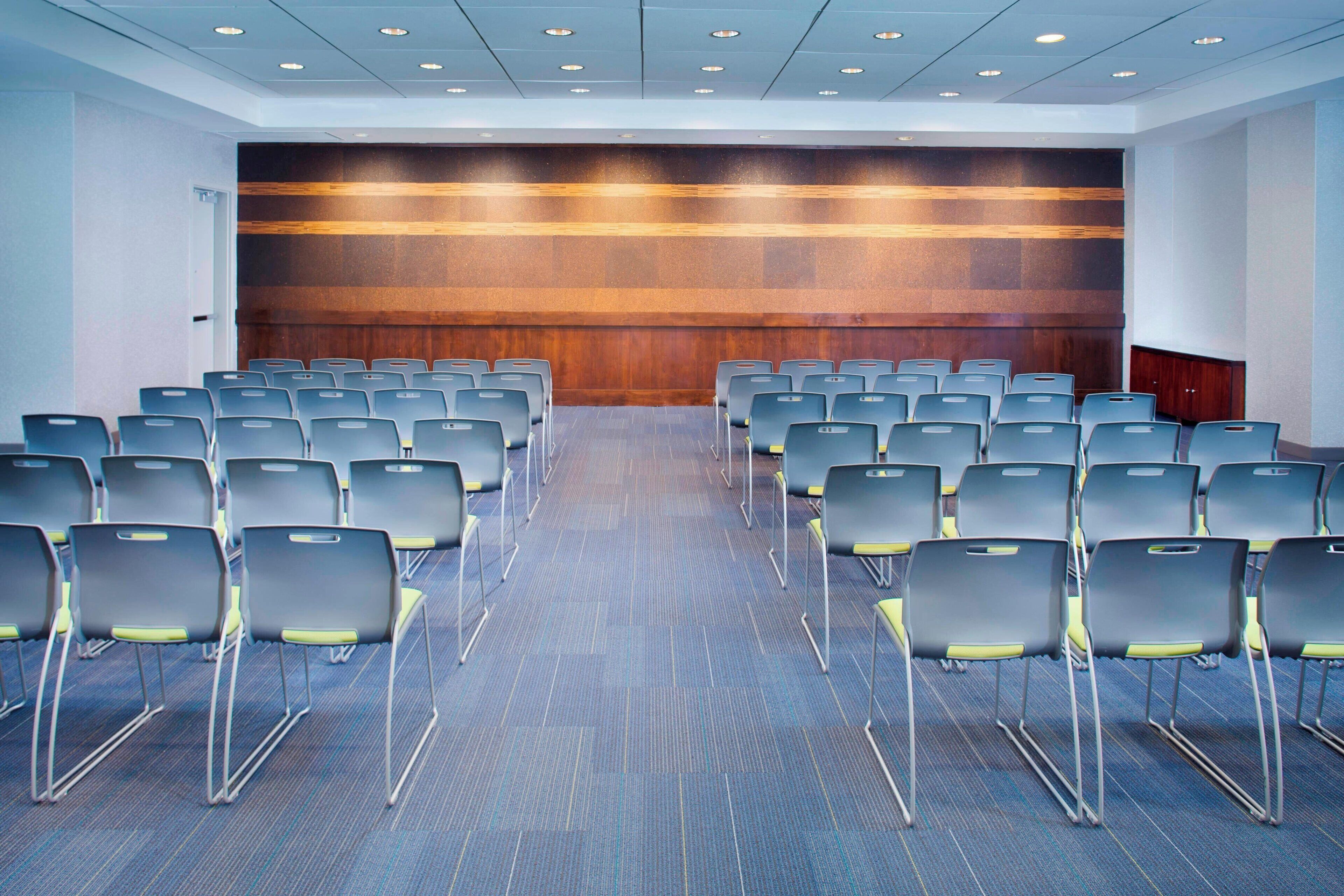 Une salle de conférence avec des rangées de chaises, un mur décoratif en bois et un sol recouvert de moquette.