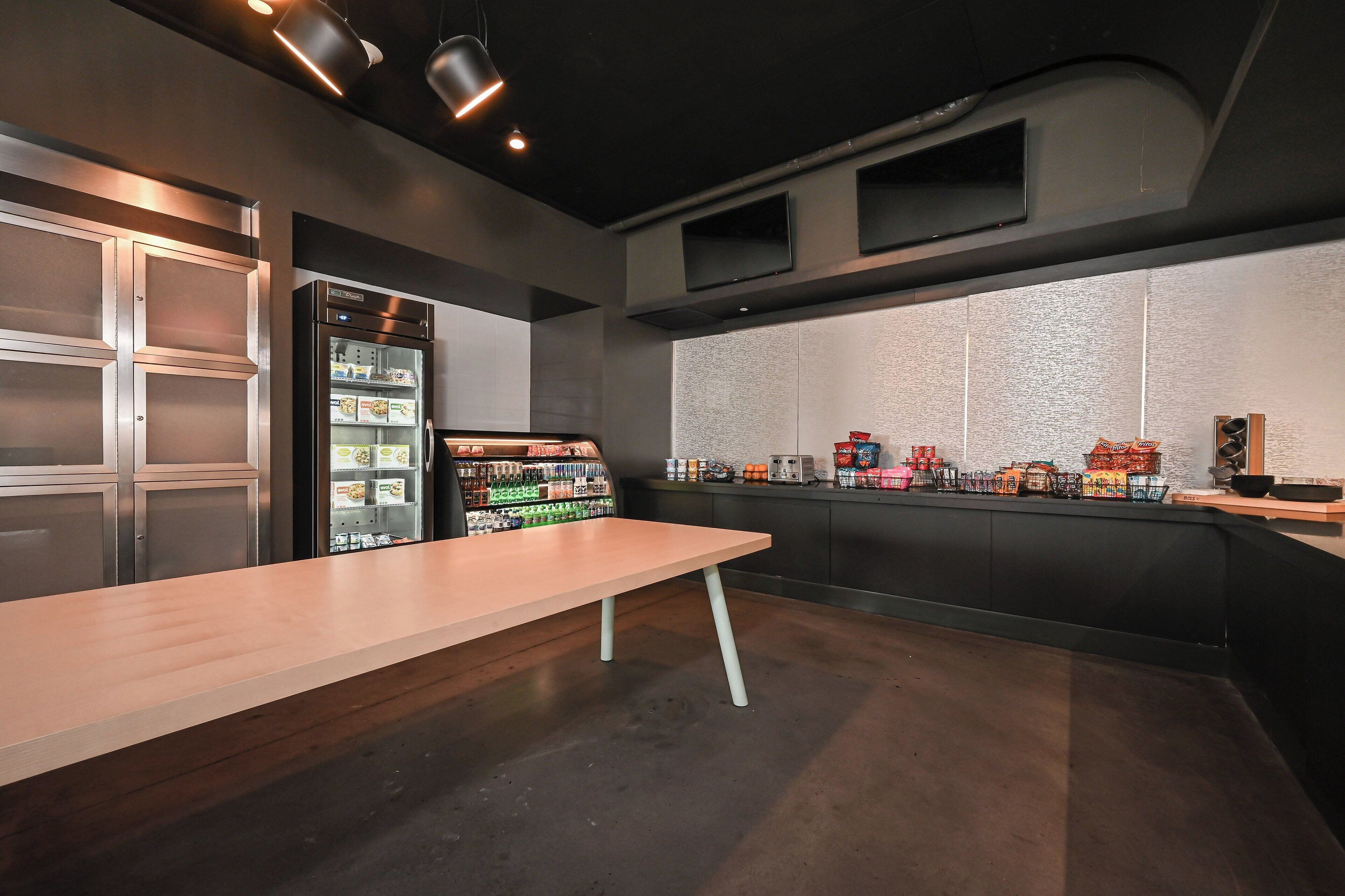 Una cocina moderna con una larga mesa de madera, un refrigerador y un expositor de aperitivos en la pared.
