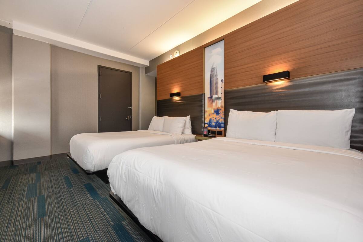 A hotel room with two beds, a wooden headboard, a cityscape mural, and a door.