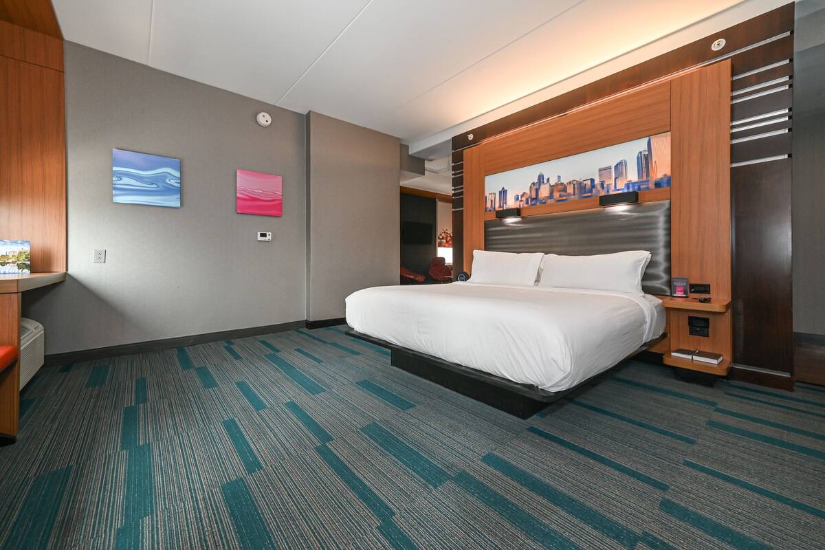 A hotel room with a large bed, a cityscape painting, and a wooden headboard.