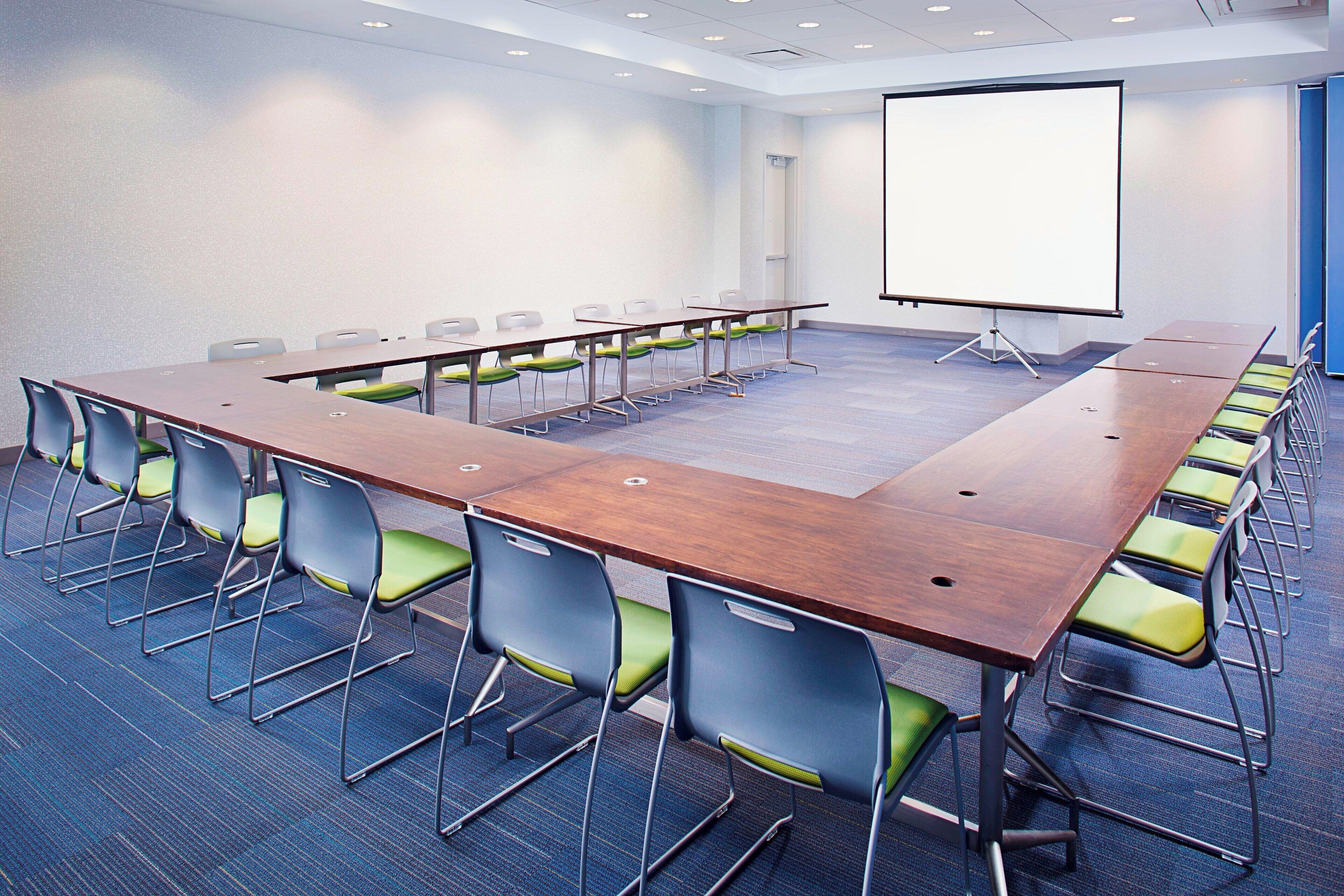 A conference room with a long table, chairs, and a projector screen.
